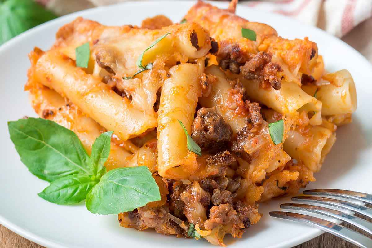 Piatto di ziti conditi con ragù di carne e foglia di basilico