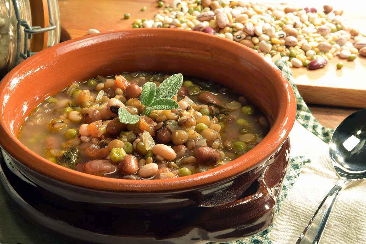 Scodella in terracotta con all'interno una zuppa di legumi decorata con delle foglioline di salvia