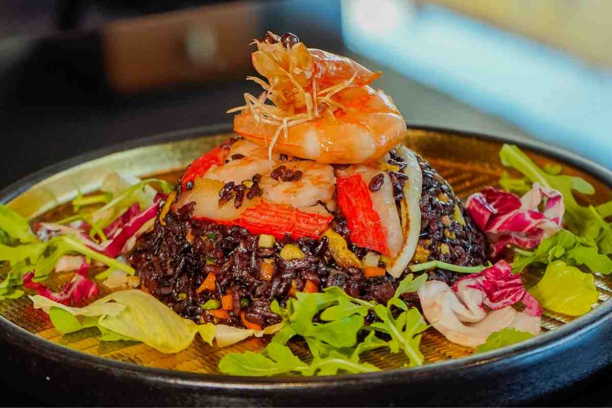 un piatto con una cupola di riso venere e frutti di mare sopra, con contorno di insalata mista