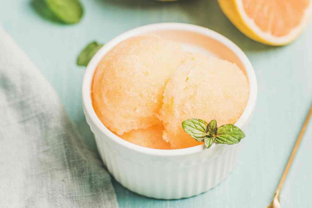 Sorbetto al pompelmo rosa in una coppetta con agrumi sullo sfondo