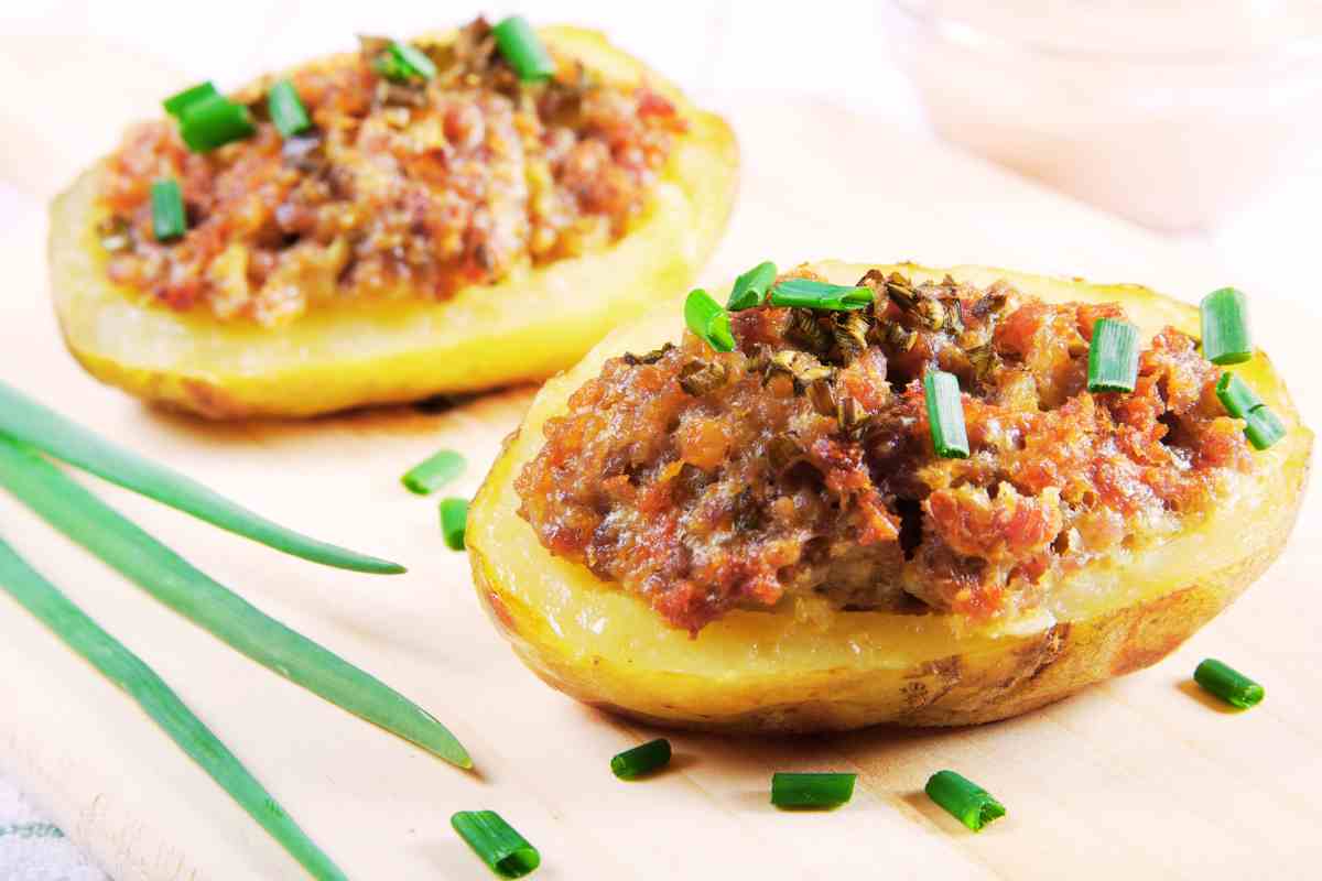 Patate ripiene di salsiccia guarnite con erba cipollina su un tagliere