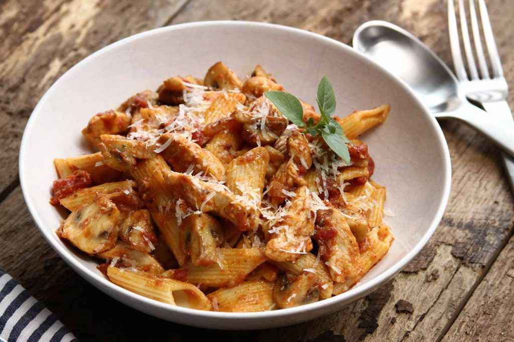 Piatto di penne con funghi, pomodoro e pancetta