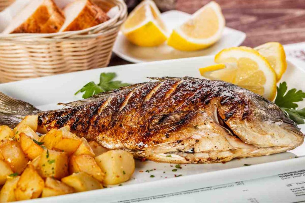 piatto rettangolare con orata al forno e contorno di patate con fette di limone di lato