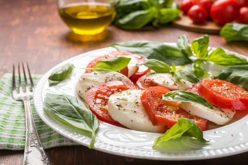 piatto piano con fette di pomodoro e mozzarella, insalata caprese con foglie di basilico