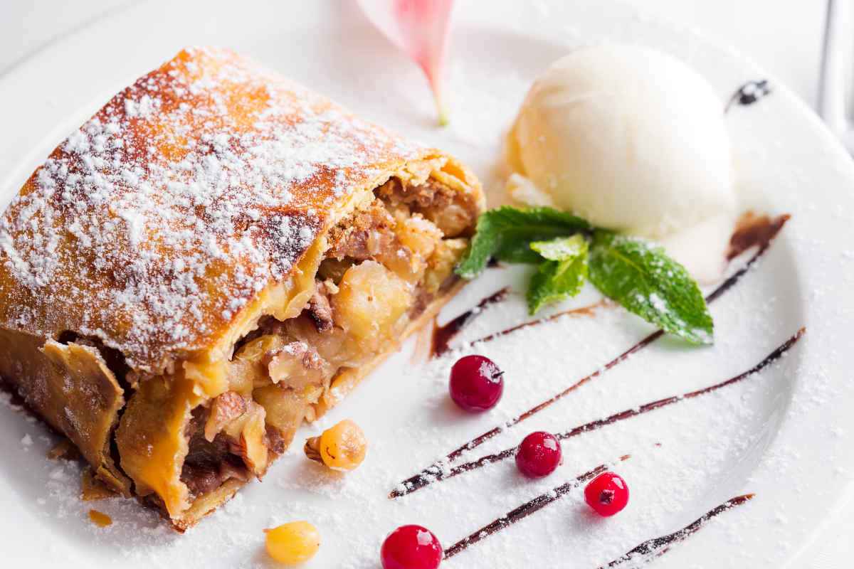 piatto bianco con fetta di strudel di mele e pallina di gelato