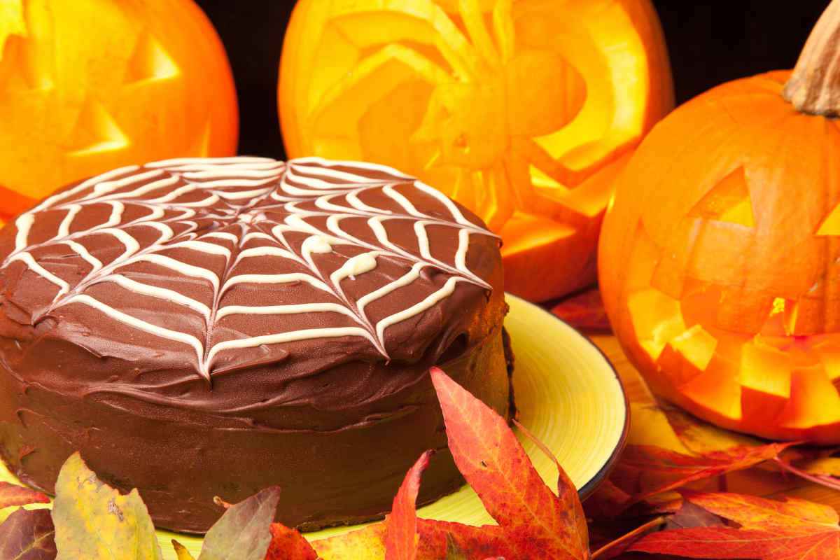 torta di halloween al cioccolato con decorazione ragnatelal vicino a zucche intagliate