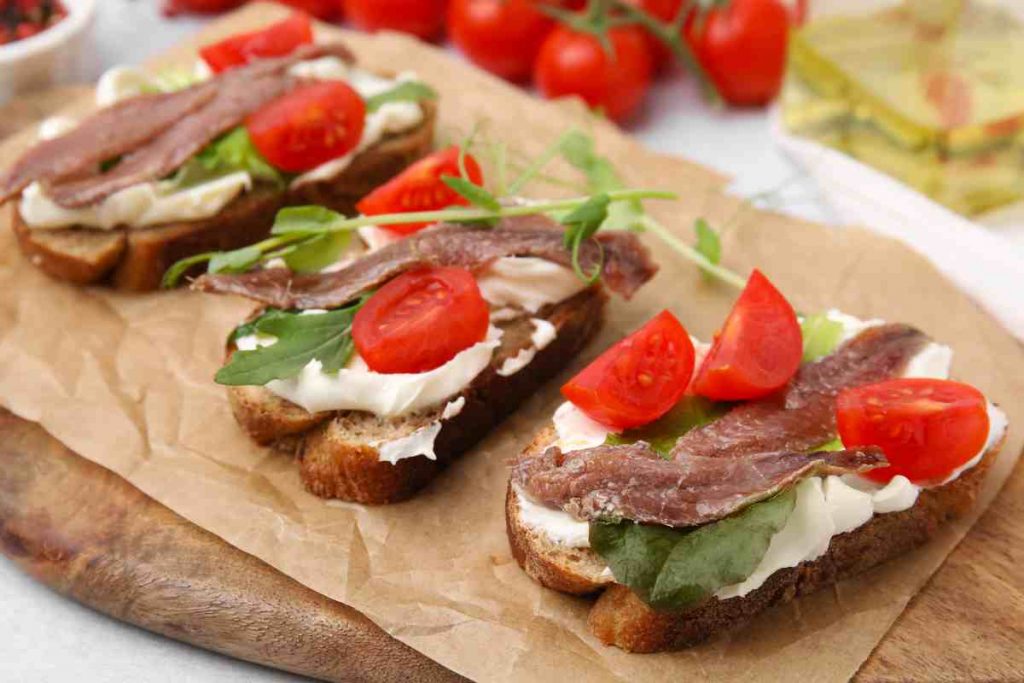 Crostini con acciughe e ricotta su un tagliere di legno