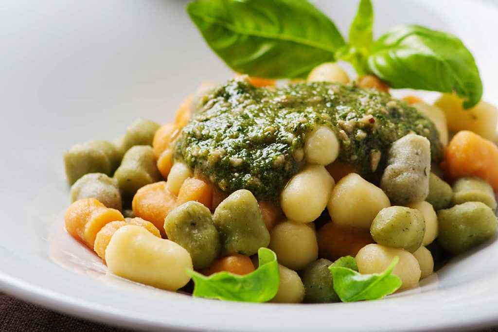 Piatto di gnocchi colorati con sugo di pesto e basilico