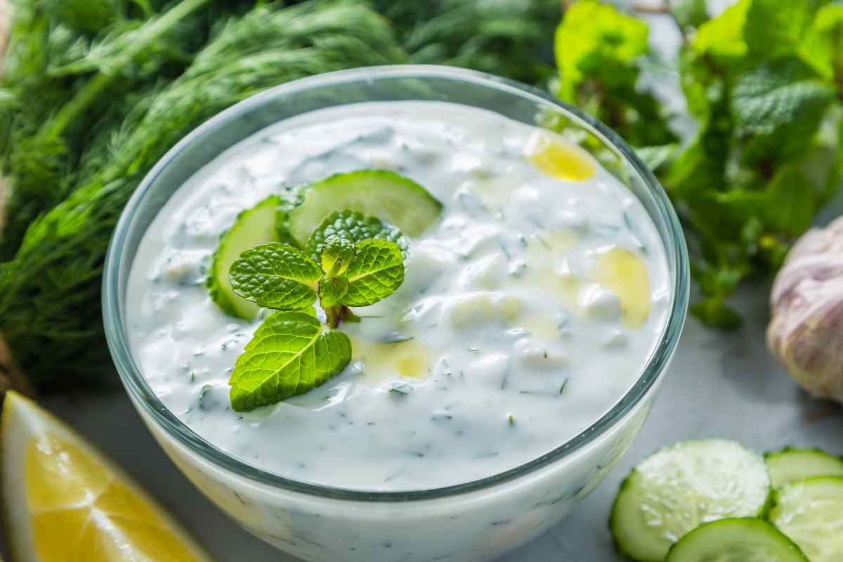 una ciotola con dentro la salsa tzatziki, fette di cetriolo e foglie di menta