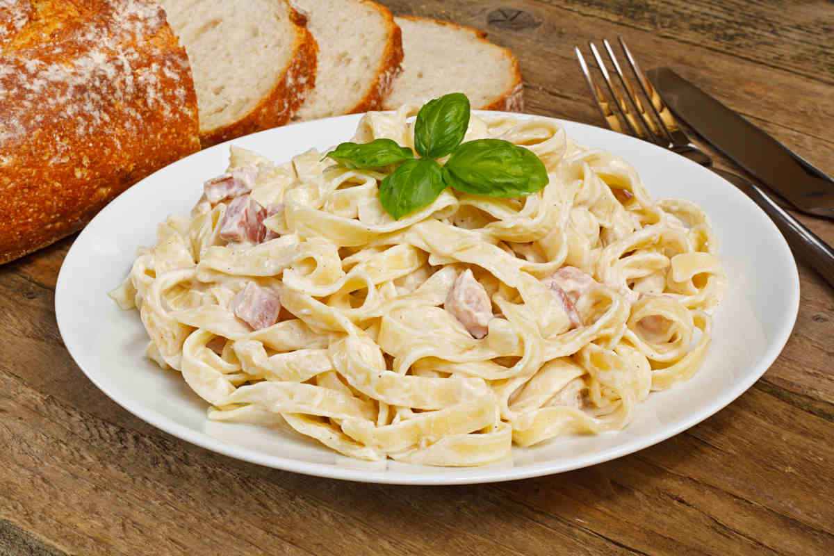 piatto da portata con tagliatelle con prosciutto crudo e foglie di basilico