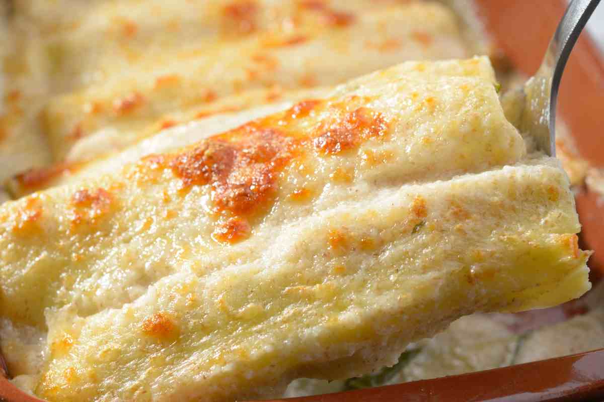 Cannelloni ai carciofi sospesi su una forchetta e sullo sfondo la pirofila