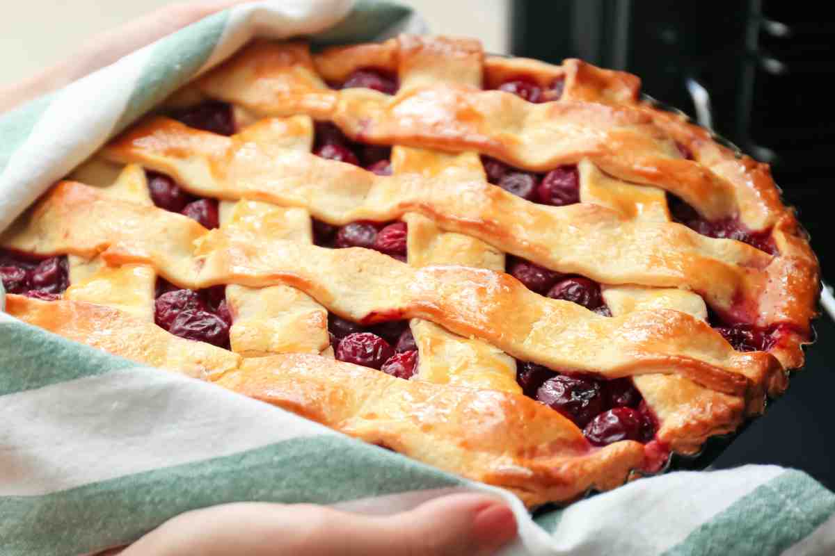 donna toglie dal forno la crostata con le ciliegie appena cotta