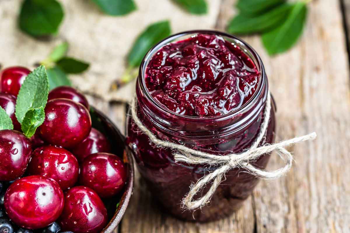 barattolo conmarmellata di amarene e frutti freschi su tavolo di legno