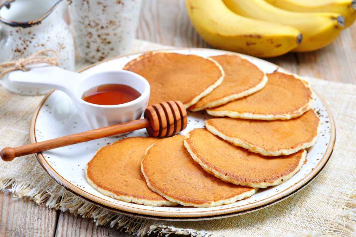 Piatto pieno di pancake senza uova con sciroppo di acero e banane