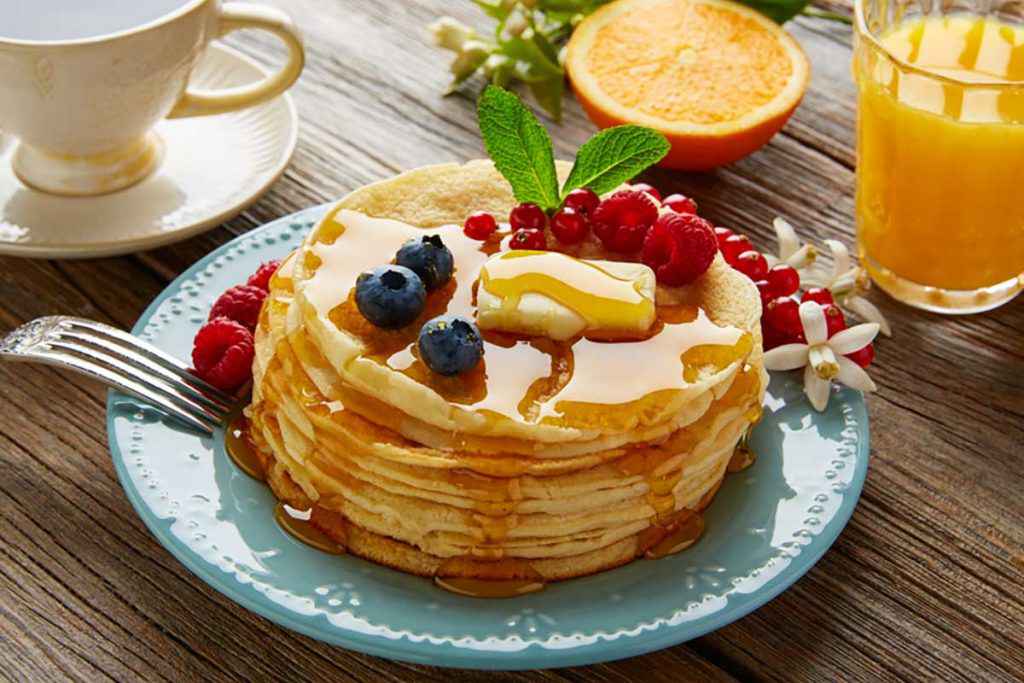 Pancake veloci con sciroppo di acero e frutti di bosco sul vassoio della colazione a letto. C'è anche la spremuta di arancia.