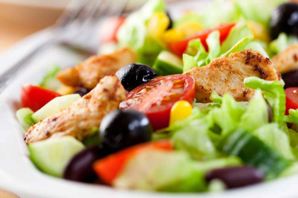 Insalata di pollo estiva con pomodori, lattuga e olive in un piatto