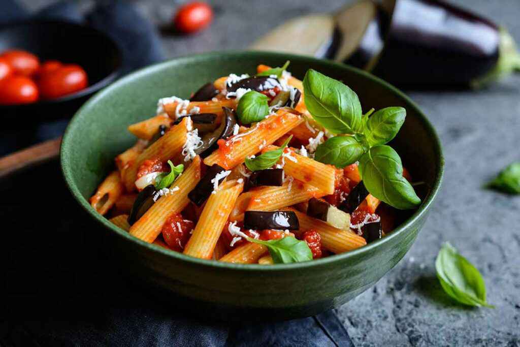 Scodella con all'interno un piatto di pasta alla Norma con melanzane, pomodori e ricotta salata