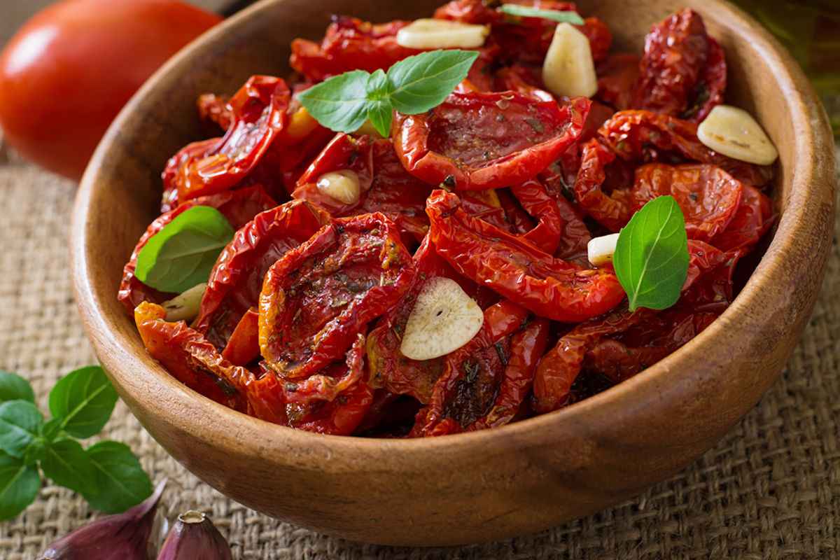 Ciotola di legno con pomodori secchi aglio e foglie di basilico