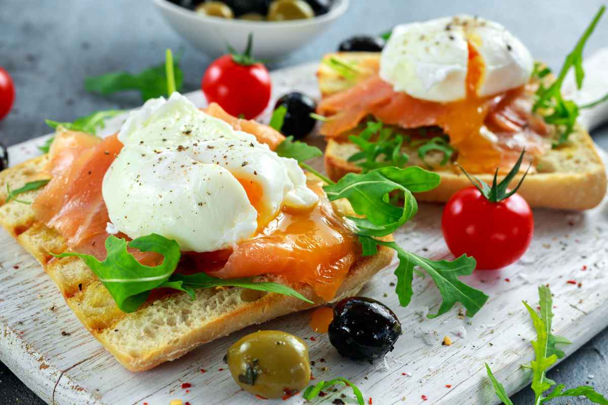 vassoio con porzioni di salmone affumicato e uova in camicia con rucola e olive