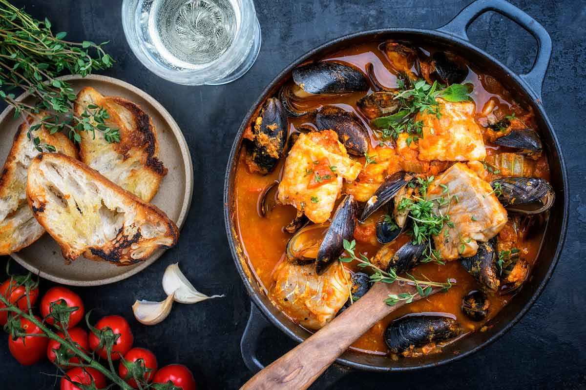 Tegame nero con all'interno una zuppa di pesce fresco servita con dei crostini di pane tostati