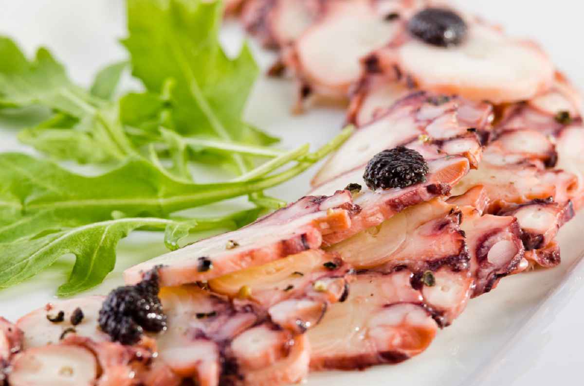 Piatto bianco con del carpaccio di polpo decorato con rucola e caviale