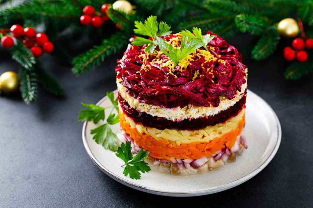 Piatto bianco con una porzione di insalata shuba e decorazioni natalizie sullo sfondo