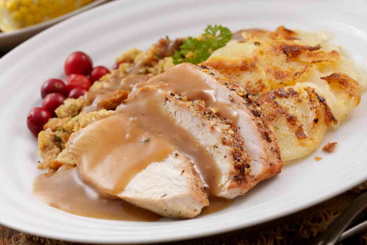 un vassoio con dentro fette di arrosto di tacchino con sughetto di verdure e patate al forno