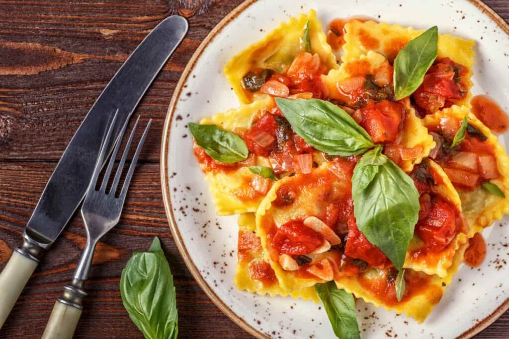 plate of ravioli in sauce with onion, cherry tomatoes and basil