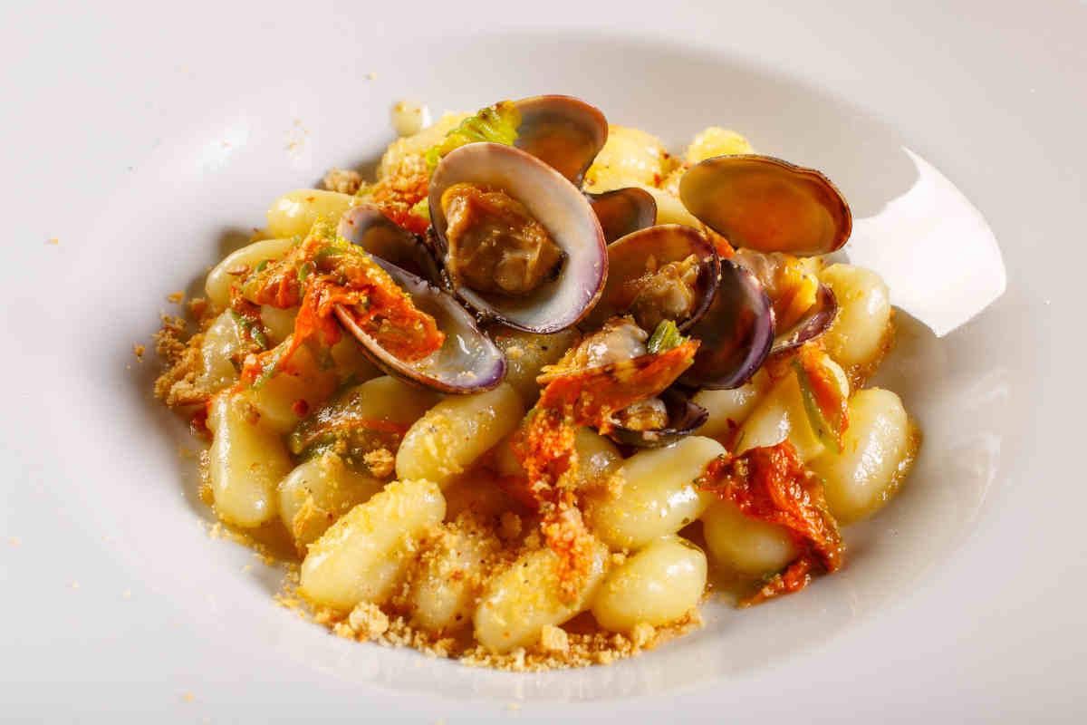 piatto fondo pieno di gnocchi con il sugo alle vongole