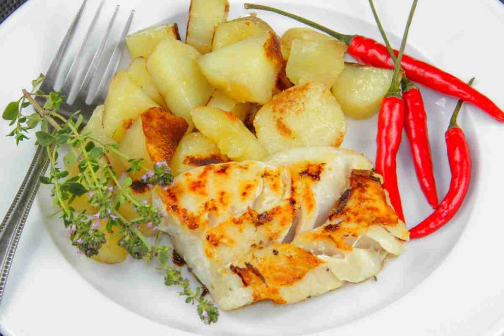Baccalà e patate al forno in un piatto guarnito con peperoncino
