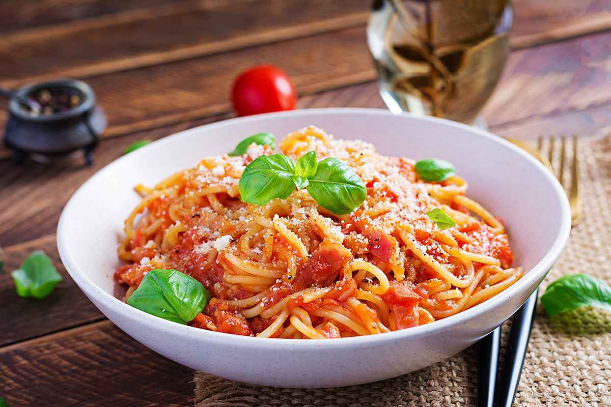 Piatto bianco con all'interno degli spaghetti conditi con sugo di pomodoro e foglie di basilico fresco