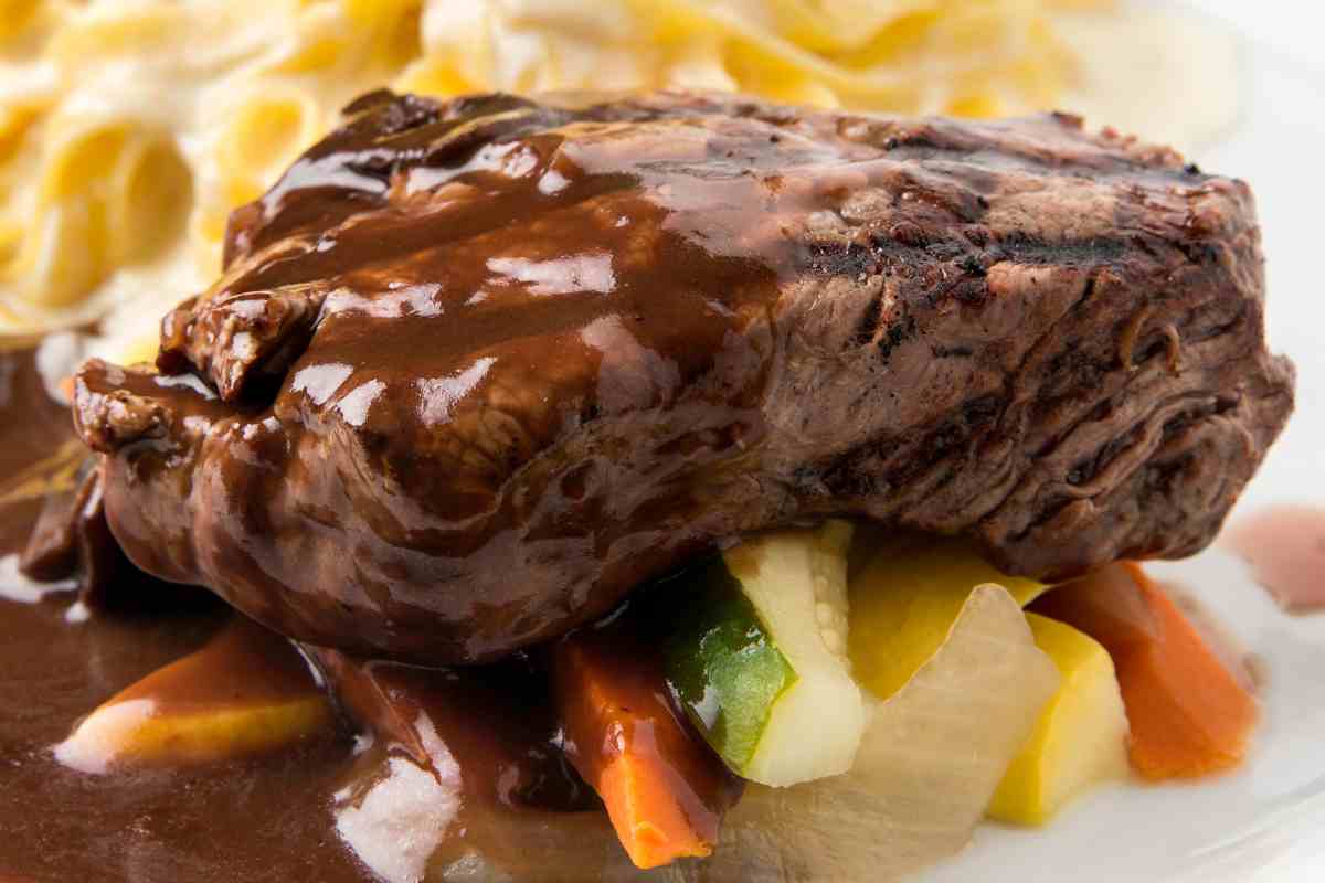 brasato al vino su un piatto con verdure e dietro delle fettuccine