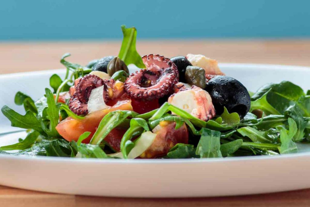 polpo con rucola, pomodori e olive in un piatto