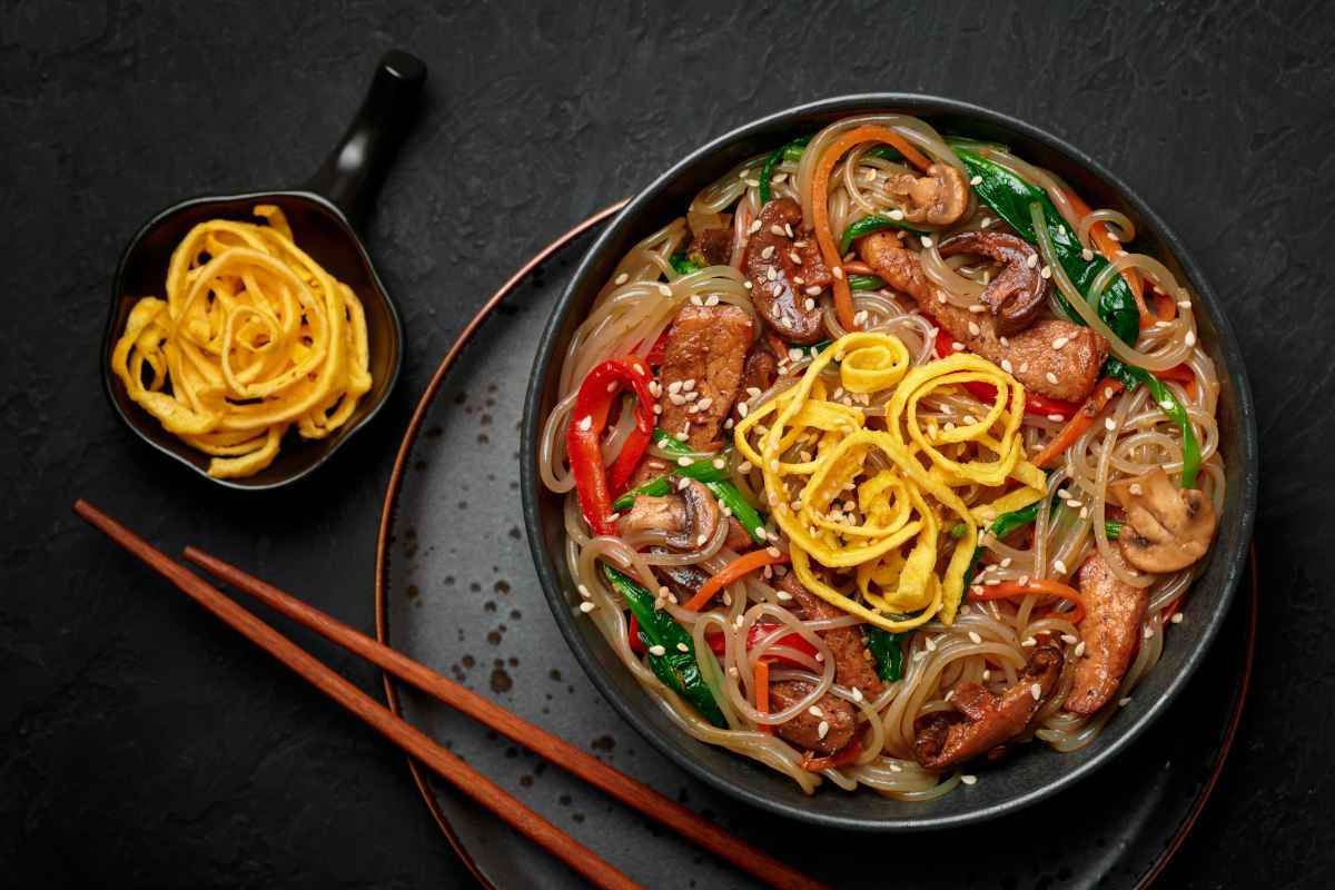 spaghetti di soia alle verdure in piatto nero con bacchette