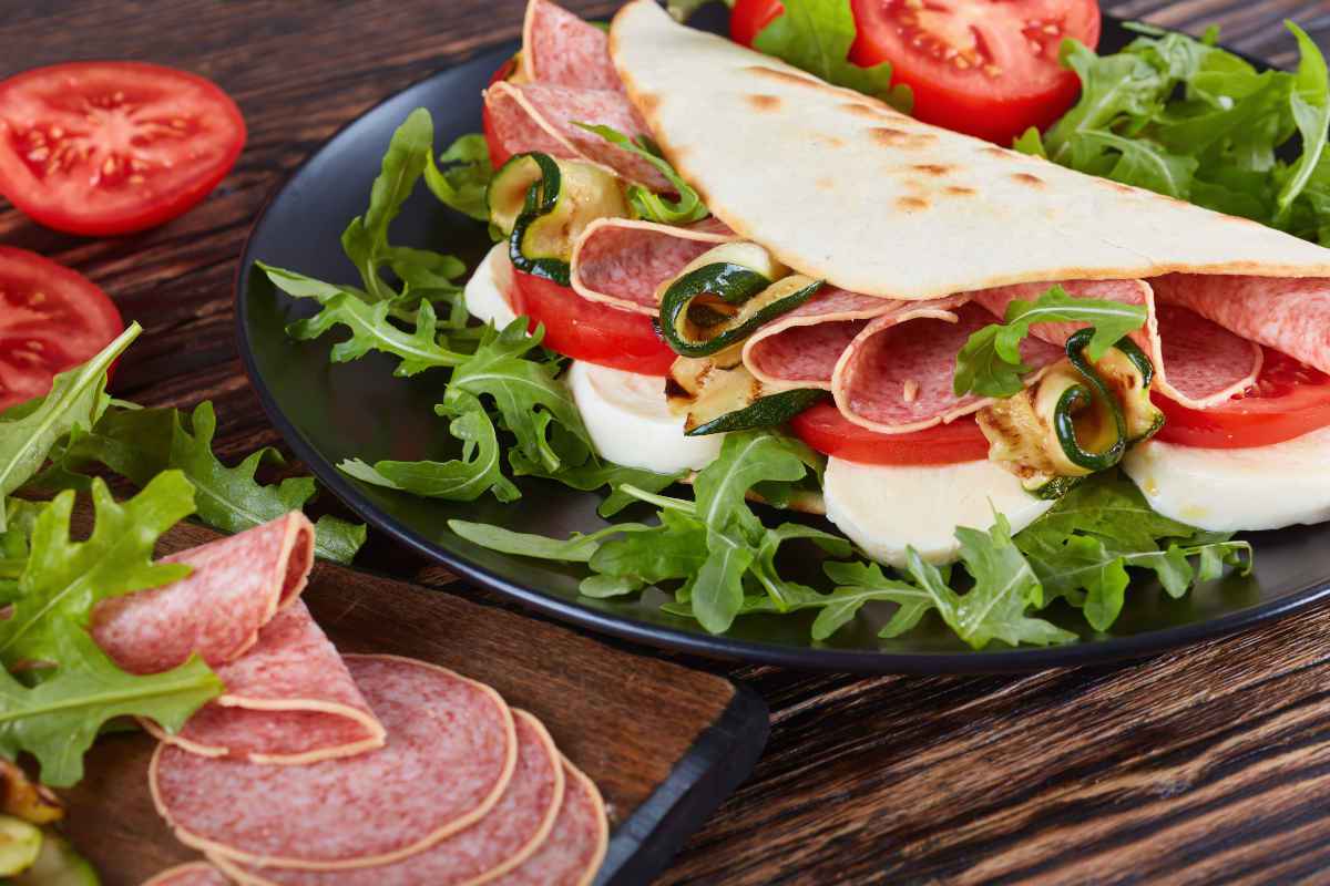 piatto nero con piadine farcite di verdure, affettati e formaggi