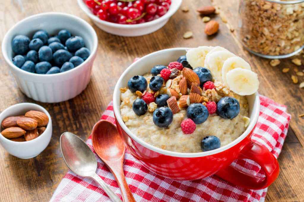 tazza rossa con porridge di fiocchi di avena e frutta secca, banane e mirtilli