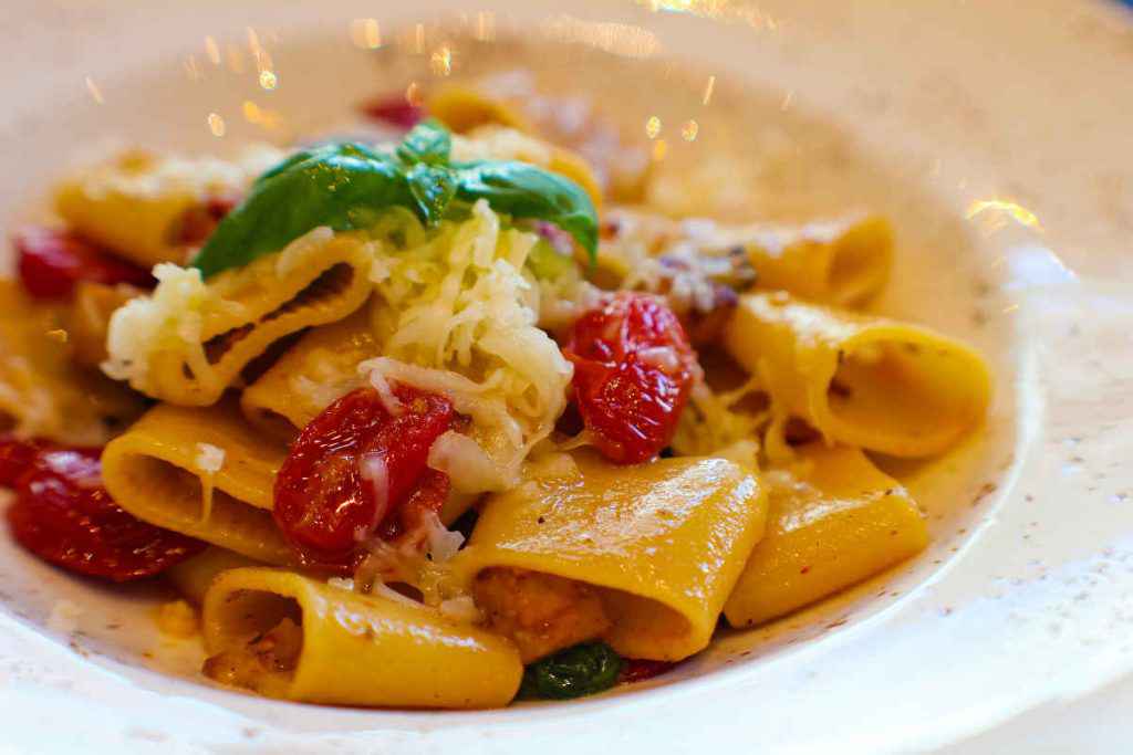 piatto di paccheri fumanti conditi con pomodorini e formaggio