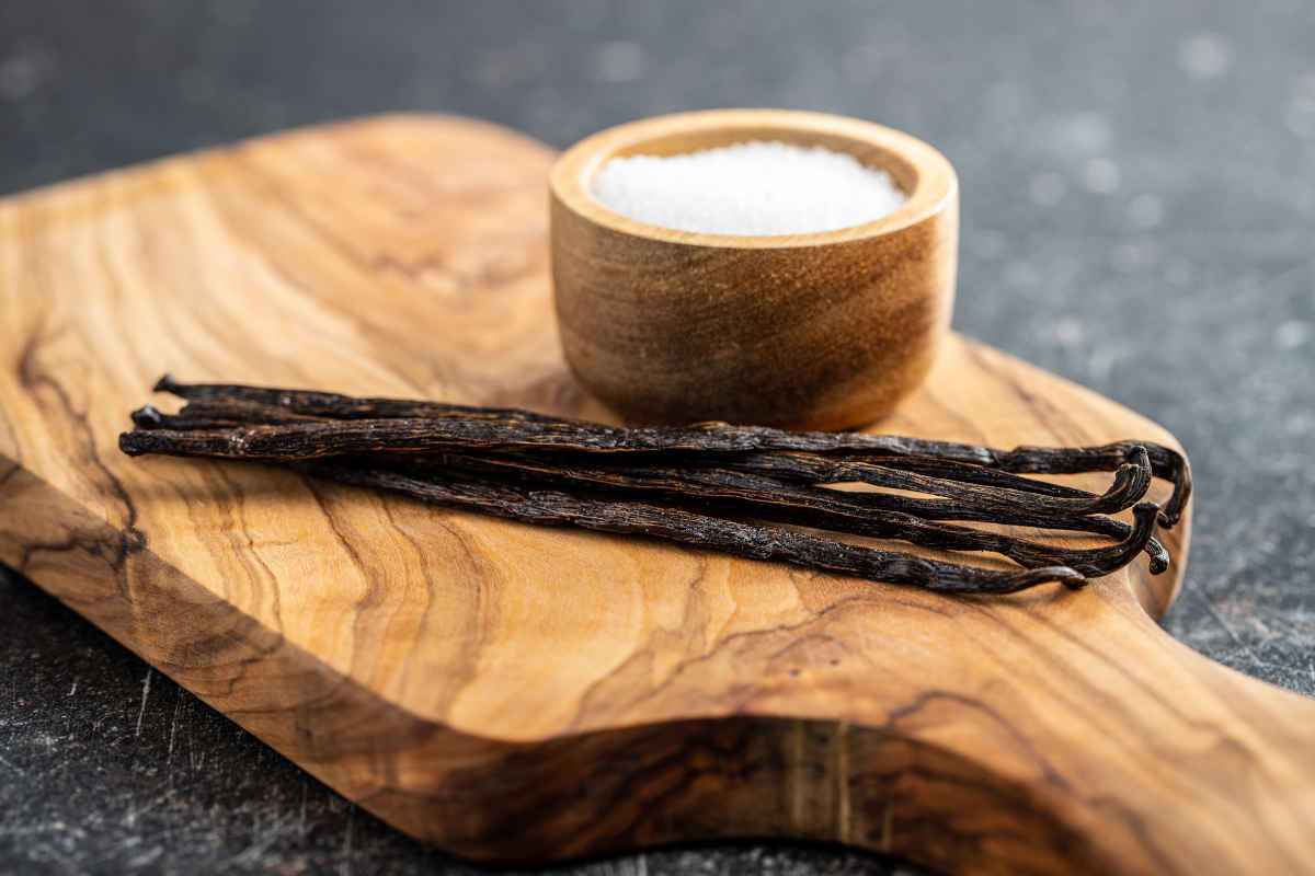 tagliere di legno con baccelli di vaniglia e ciotolina di sale