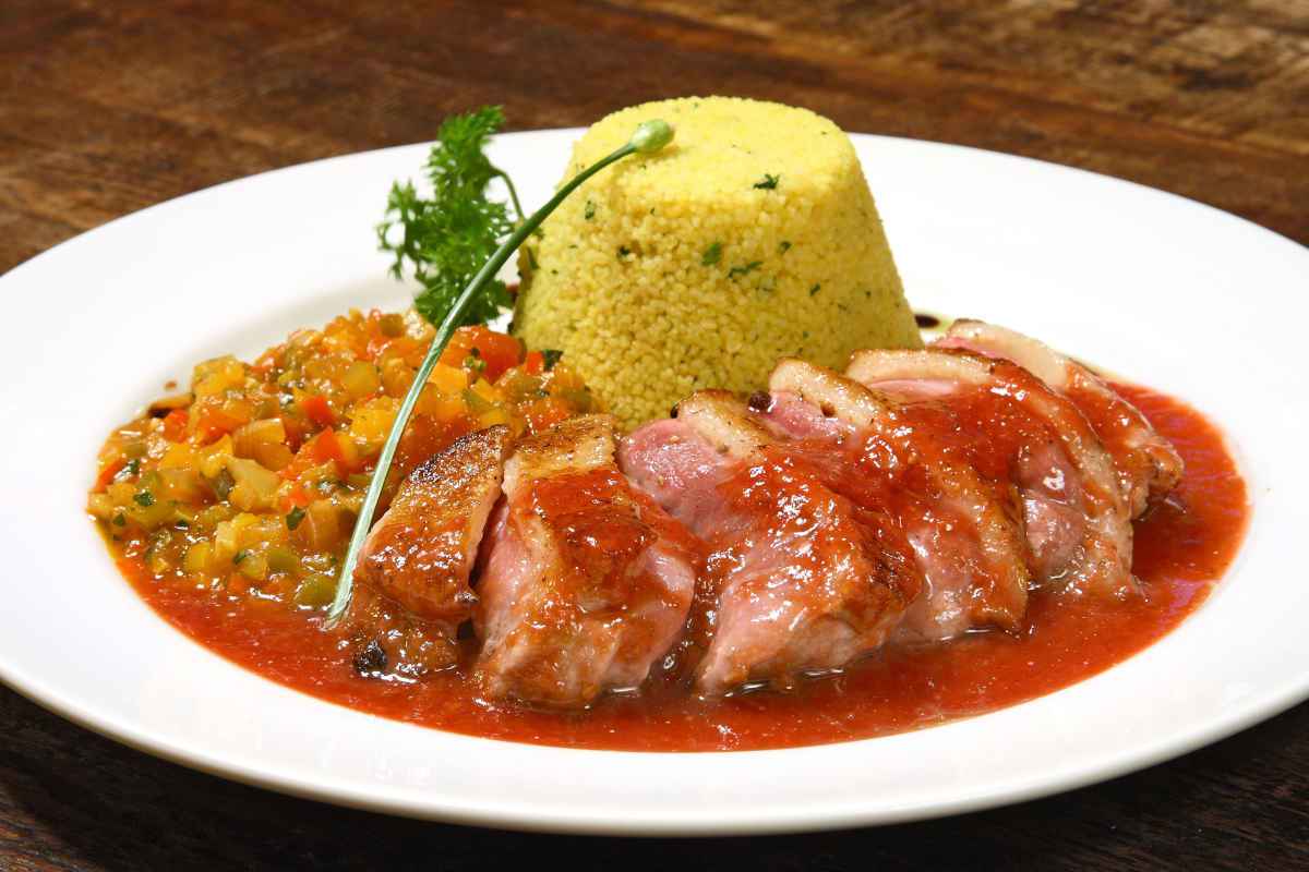 piatto con carne di maiale condita con salsa agrodolce e contorno di cous cous e verdure