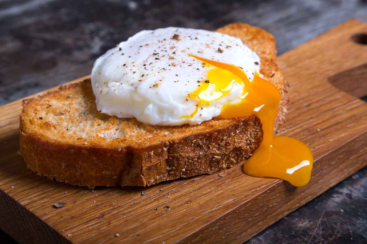 Fetta di pane abbrustolito su cui sopra c'è un uovo in camicia con tuorlo fondente