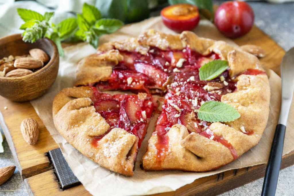 tagliere di legno con sopra una crostata di prugne fresche fatta con la pasta brisè