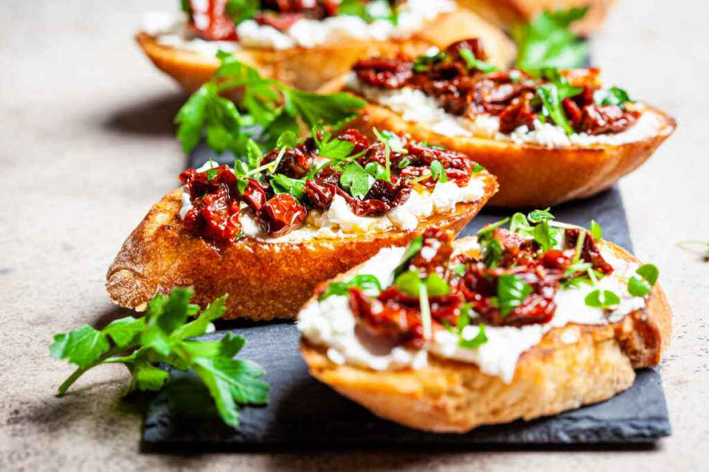 bruschette con formaggio e pomodori secchi su tagliere di ardesia