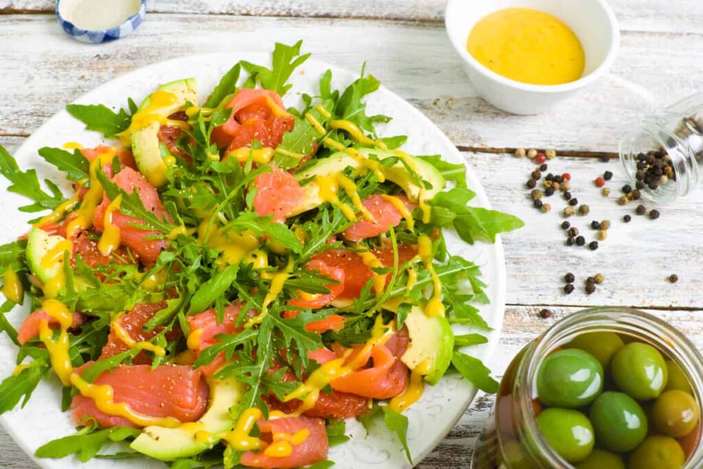 Piatto con carpaccio di salmone rucola e avodado accanto ciotolina con olive