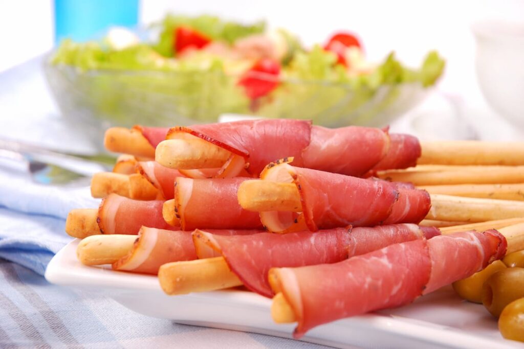 vassoio grissini con mousse di tonno e prosciutto crudo accanto ciotola con insalta