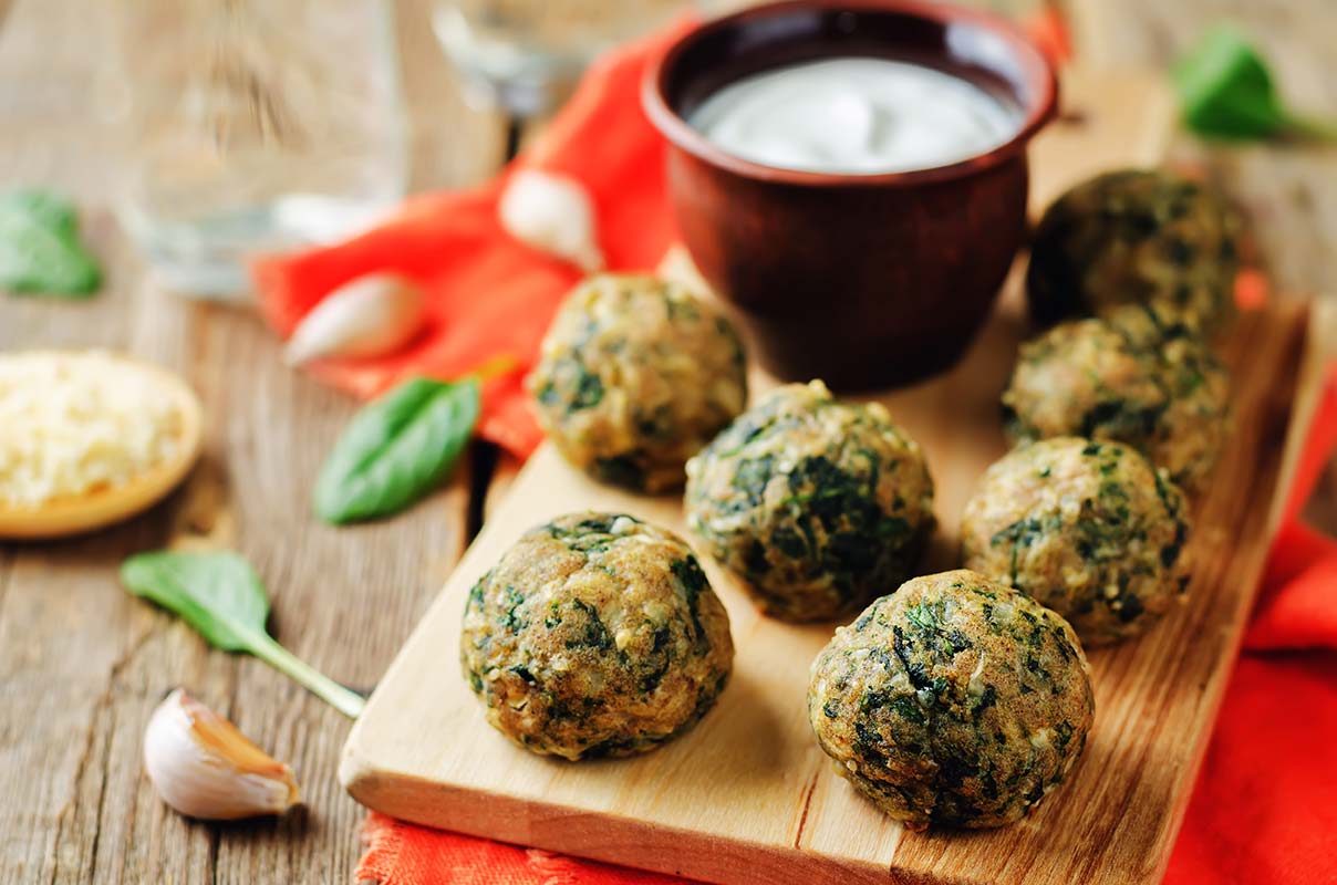 Tagliere di legno con sopra delle polpette di spinaci e una ciotolina di salsa bianca allo yogurt