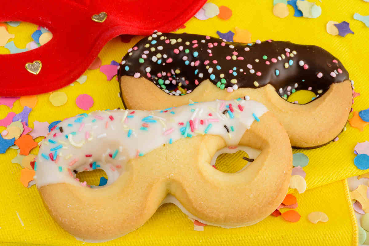 tavola colorata con sopra dei biscotti di carnevale a forma di maschera con cioccolato e zuccherini