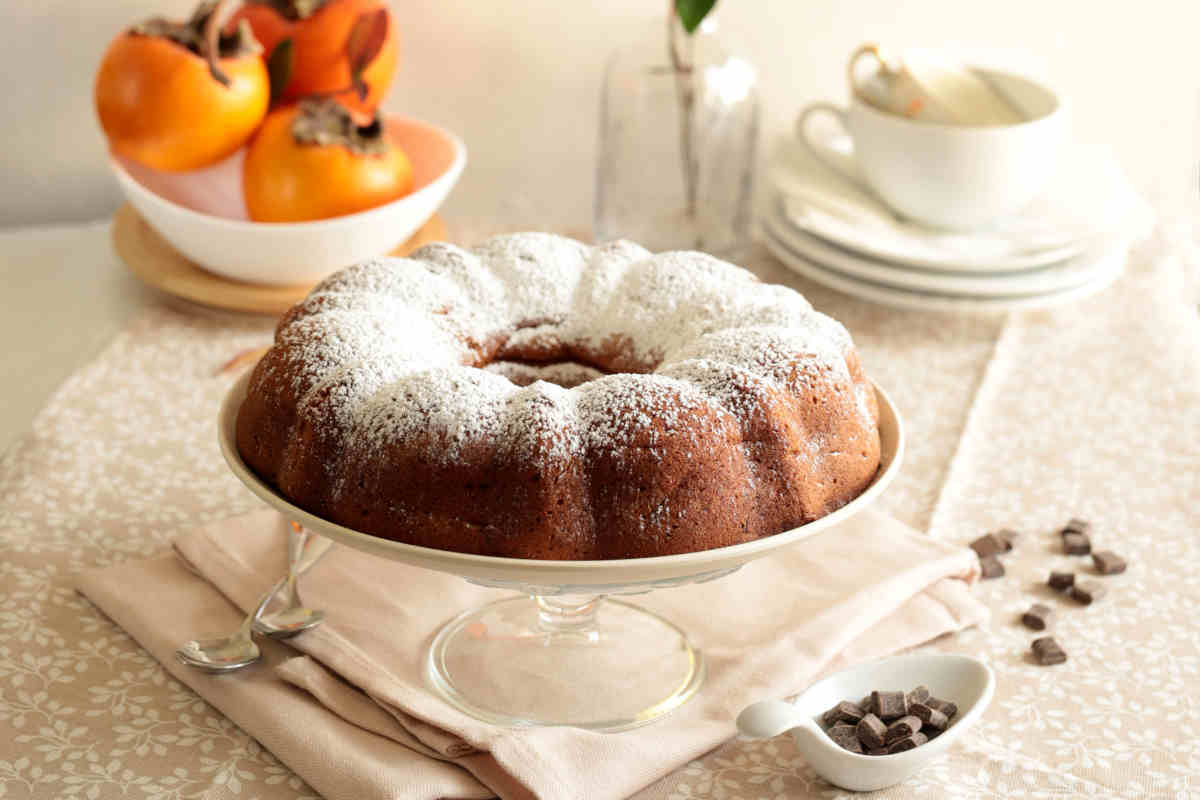 alzatina con torta ai cachi e frutti sullo sfondo