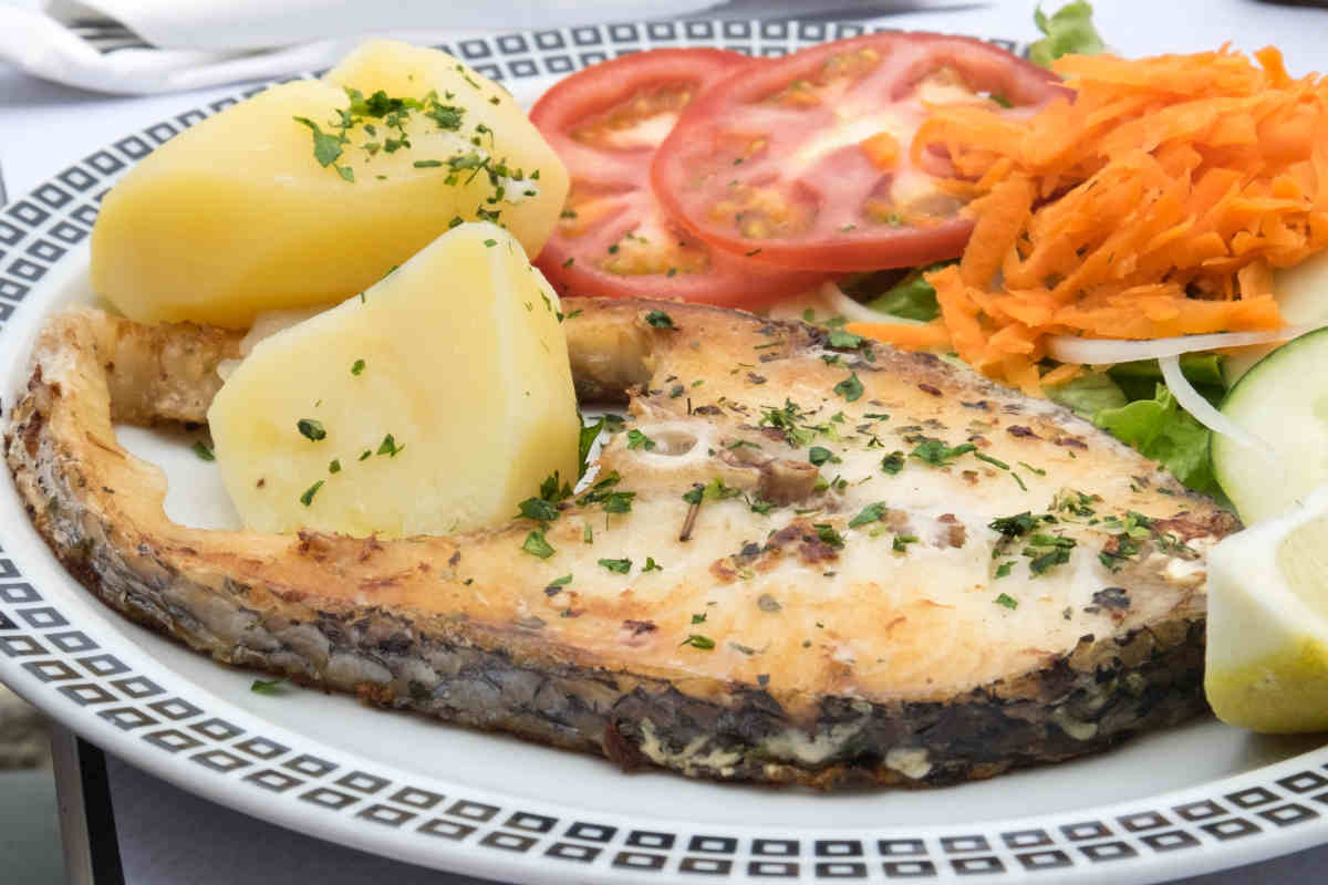 Piatto con trancio di pesce spada al forno e contorno di patate e pomodori