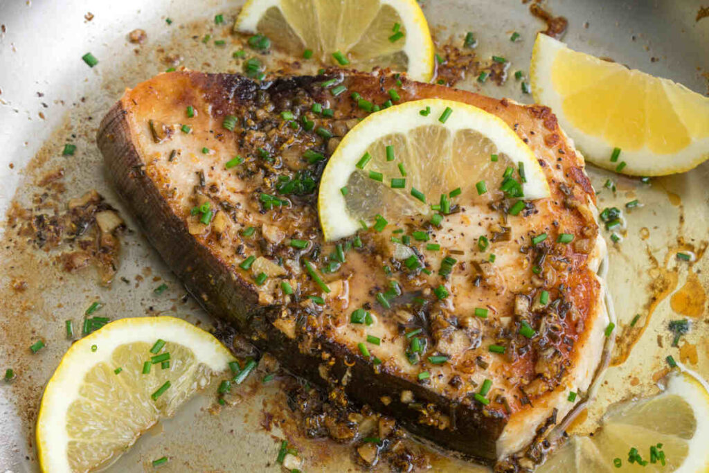 fetta di pesce spada al limone con fondo di cottura all'interno di un piatto