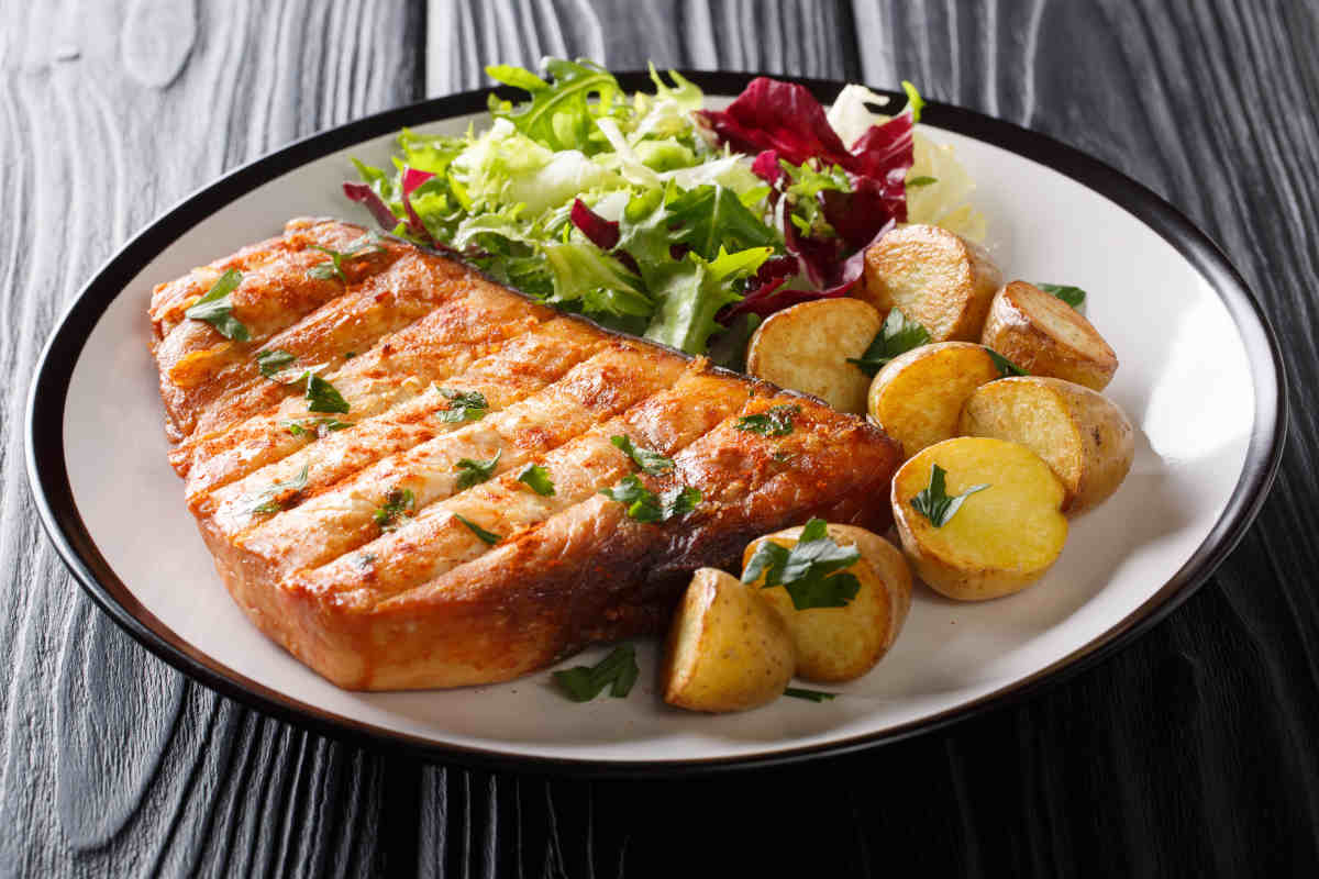 piatto con fettina di pesce spada grigliato alla piastra e insalatina verde con patate al forno